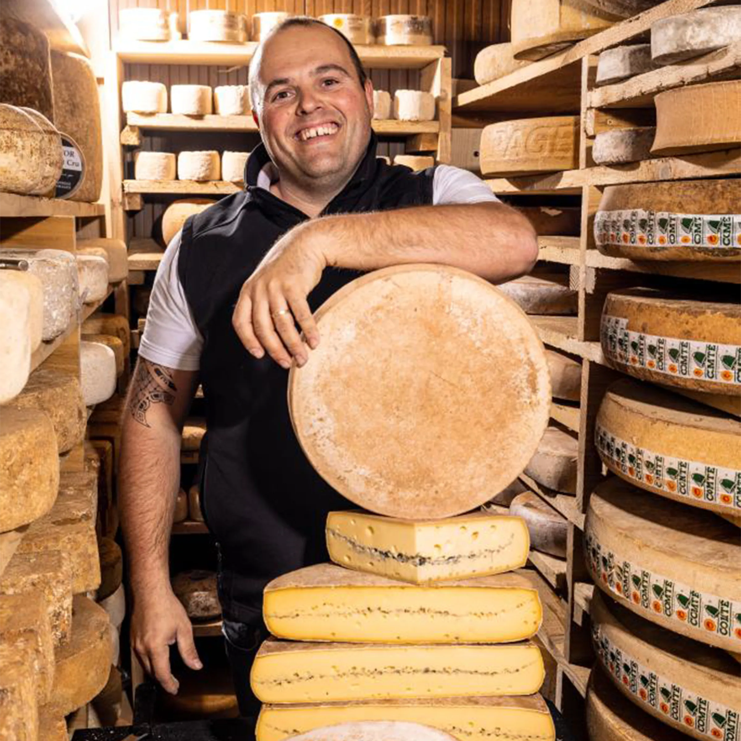 Freddy, fromager affineur, souriant dans sa cave d'affinage au milieu des meules