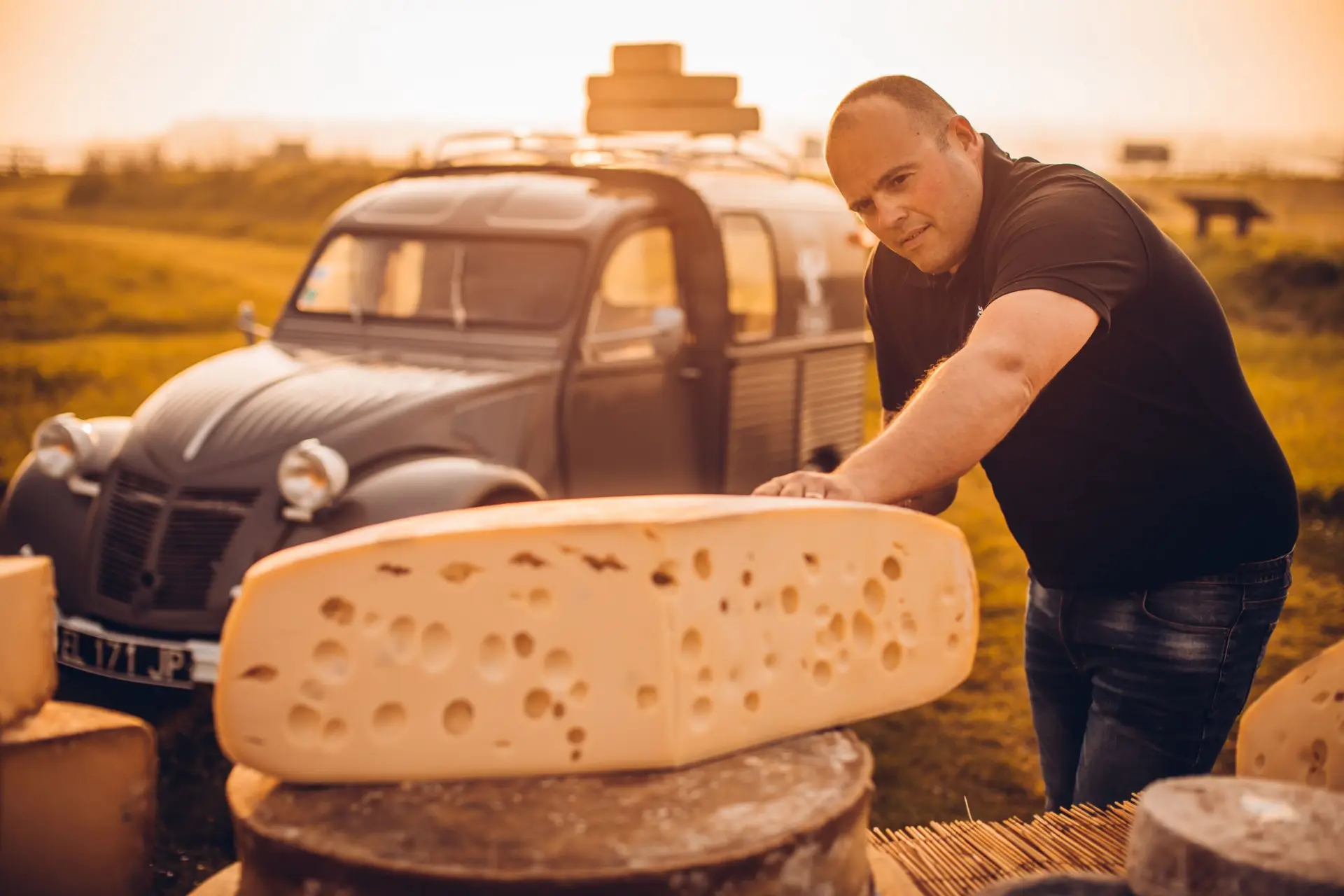 Freddy, la main posée sur une grande meule de fromage, devant une 2CV chargée de meules